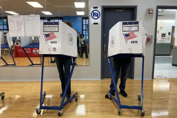 Two people's legs visible under voting booths at Eleanor Roosevelt High School on the Upper East Side.